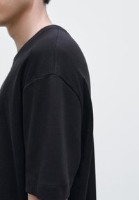 Svart bomullst-shirt med avslappnad passform, korta ärmar och rund halsringning. Mjuk textur och minimala sömdetaljer.