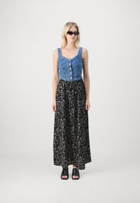 Top sans manches en denim avec fermeture à boutons, associé à une jupe maxi noire à motifs floraux et des chaussures noires à bout ouvert.