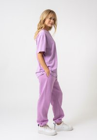 Lavandas kokvilnas T-krekls ar īsām piedurknēm apvienots ar atbilstošām sporta biksēm. Sporta biksēm ir sānu kabatas un elastīgas aproces. Masīvas baltas kedas.