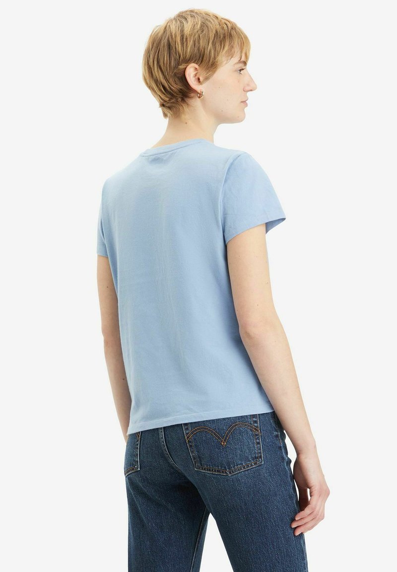 Helles blaues Baumwoll-T-Shirt mit kurzen Ärmeln, Rundhalsausschnitt und lässigem Schnitt, kombiniert mit dunkelblauen Jeans, die ein auffälliges Design der Gesäßtasche aufweisen.