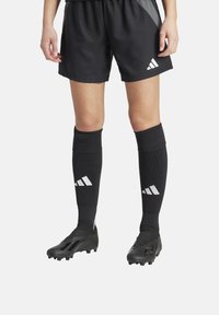 Zwarte voetbalshorts met een gestructureerd ontwerp, gecombineerd met zwarte kniekousen met witte Adidas-strepen en zwarte voetbalschoenen met een slank profiel.