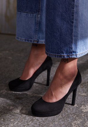 Schwarze Wildleder-Pumps mit abgerundetem Zehenbereich und Plateau-Iso, kombiniert mit weitem Denim mit kontrastierendem Saum.