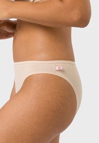 Nude hochtaillierte Panties aus glattem Material, mit einem kleinen rosa Logotag an der Seite und nahtlosen Kanten für zusätzlichen Komfort.