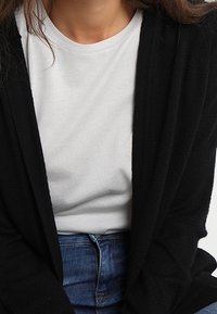 Black cardigan made of soft fabric, layered over a light gray t-shirt, paired with blue jeans. Simple design with no visible patterns.