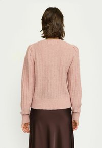 Lichtroze gebreid truitje met geribbelde textuur, pofmouwen en een ronde halslijn, gedragen over een bruine zijden rok.