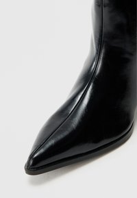Čierna kožená členková čižma s výraznou špičkou, hladkým povrchom a minimalistickým dizajnom. Vyznačuje sa štíhlym siluetom a jemným šitím.