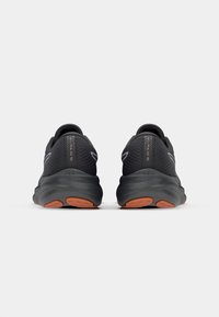 Baskets de sport noires avec une tige en mesh texturé, semelle extérieure orange contrastante et cols rembourrés, arborent un design épuré et des accents minimaux.