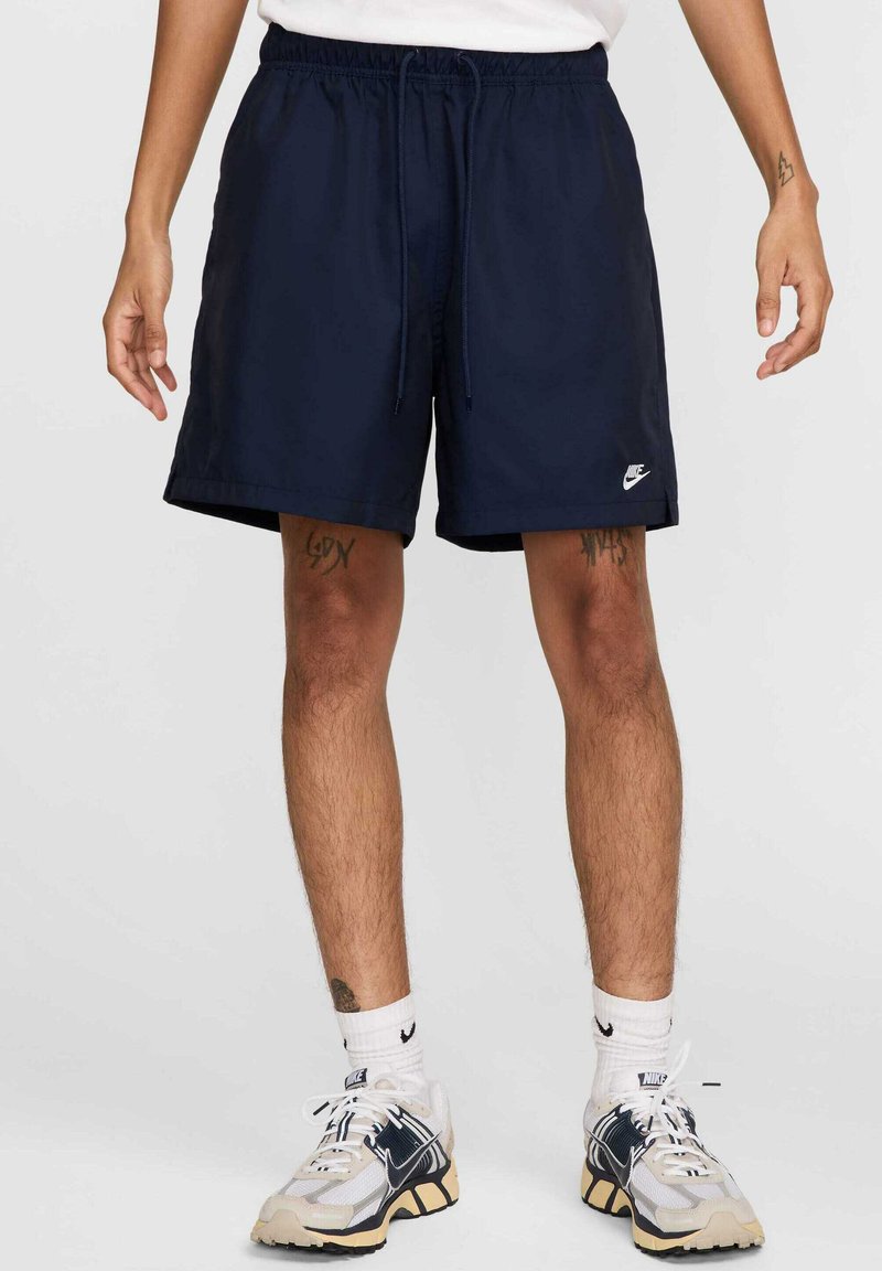 Granatowe szorty Nike z elastycznym pasem i sznurkiem. Materiał jest gładki, z małym białym logo w kształcie swisha na dolnej krawędzi.