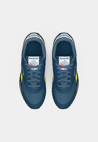 Mėlyna ir geltona Reebok sportbačių pora, matoma iš viršaus ant baltos fono, su pilkais raiščiais ir Reebok logotipu ant liežuvėlių.