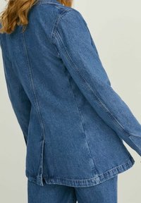 Džínová bunda světle modré barvy, s rovnými liniemi, dlouhými rukávy a detailem zadního švu. Měkká textura s lehce vybledlým vzhledem.