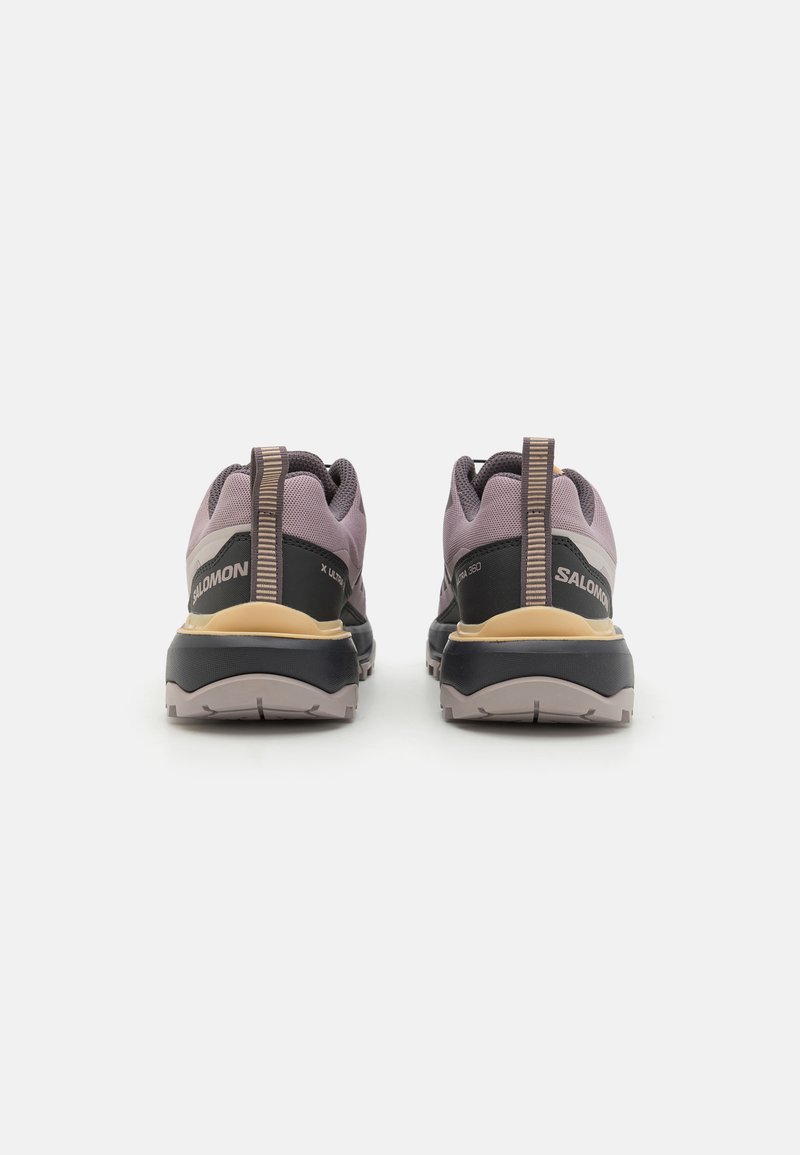 Zapatos de exterior en púrpura y negro con una parte superior de malla texturizada, tirador trasero y una suela de goma duradera. Presenta una marca en el talón.