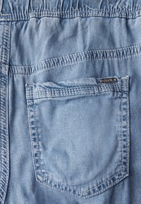 Jasnoniebieskie dżinsy z marszczonym pasem, pojedynczą kieszenią z tyłu i małą metalową metką oznaczoną "Cecil". Gładka faktura z widocznym przeszyciem.