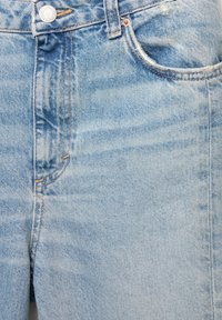 Jasnoniebieskie dżinsy mają klasyczny pięciokieszeniowy design, z żółtym przeszyciem i metalowym zapięciem w pasie.