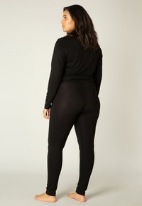 Zwart langarmpoltop en legging set gemaakt van gladde, rekbare stof. Heeft een aansluitend ontwerp, minimale naden en een naadloze tailleband.