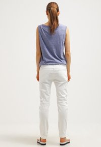 Top azul sin mangas con un ajuste holgado, combinado con jeans blancos de corte ajustado. Se lleva con sandalias informales, mostrado desde la parte de atrás contra un fondo neutro.
