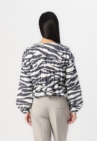 Blusa às riscas preto e branco com detalhes franzidos na cintura, mangas bufantes e uma barra cropped, combinada com calças beije de corte clássico.