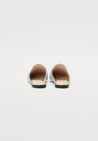 Sølvmetalliske slip-on leiligheter med åpning bak, glatt tekstur og flate svarte såler. Minimalistisk design, uten pynt og uten maskinvare.