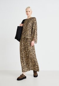 Leopardmønster antrekk med en løs topp og lang skjørt, begge i beige med svarte prikkar. Svart slip-on sko og en svart kviltet veske.