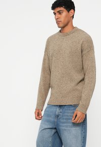 Vaaleanbeige neulepaita pyöreällä pääntiellä ja ribattu helma. Sisältää tekstuuripinnan ja pudotetut olkatikkaukset, yhdistettynä vaaleansinisiin farkkuihin.