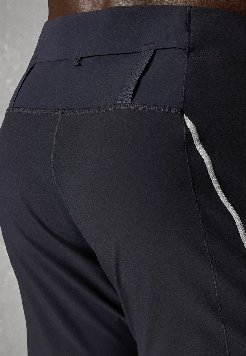 Gros plan sur une personne portant un pantalon de sport noir avec une taille haute et un petit détail en boucle noire à l'arrière.