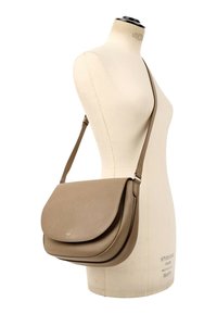 Sac bandoulière en cuir beige avec fermeture à rabat présenté sur un mannequin forme robe couleur crème.