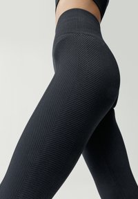 Vysoké čierne legíny s rebrovanou a rybí kosťou textúrou, s hladkým, elastickým materiálom, ktorý sa prispôsobuje telu.