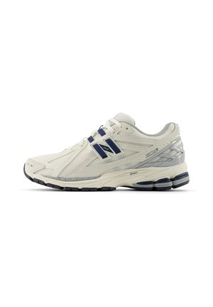 Zapatilla deportiva New Balance 1906R en crema y gris con acentos en azul marino y suela con amortiguación detallada, mostrada desde el lado exterior.