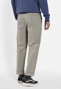 Grå skräddarsydda byxor med en slät yta, uppvikta fållar och två bakfickor, matchade med svarta sneakers och en marinblå tröja.