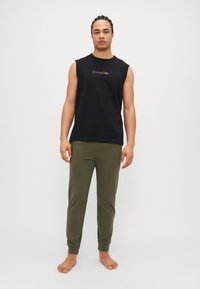 Svart ermeløs skjorte med "Calvin Klein"-logo i fargerik skrift, parret med olivengrønne joggebukser med ribbede mansjetter.