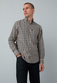 Chemise à manches longues avec boutons, présentant un motif à carreaux beige et marine, fabriquée en tissu doux, avec un ourlet arrondi et une poche poitrine.