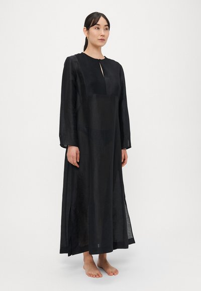 Rochie lungă neagră dintr-un material ușor, cu guler înalt, detaliu plisat în față și despicături laterale, cu mâneci lungi.