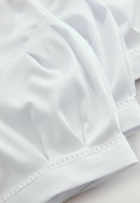 Tessuto bianco con una superficie liscia, caratterizzato da sezioni arruffate e bordi in pizzo lungo l'orlo, che creano una caduta morbida e rilassata.