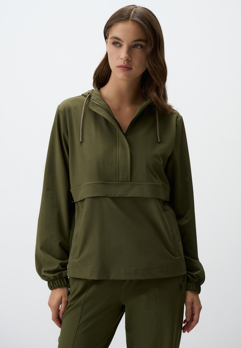 Pull olive avec capuche, demi-fermeture éclair à l'avant et poignets élastiques. Présente une couture horizontale au niveau de la poitrine et des poches latérales.