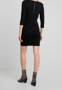 Mustapohjainen mekko, jossa on kolme neljäsosapituista hihaa, teksturoitu kangas, takana vetoketjun sulku ja reiden puoliväliin ulottuva pituus. Yhdistetty käärmeennahkakuosisilla saappailla.