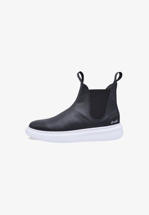 Botas Chelsea de cuero negro con paneles elásticos en los laterales, suela de goma blanca y lengüetas para facilitar el calzado. Textura suave con un diseño minimalista.