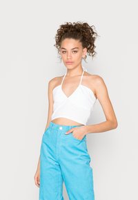 Top halter branco curto com decote em V e franzidos na busto, combinado com calças de veludo cotelê leves e azul claro de cintura alta.