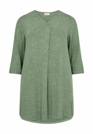 Vihreä pitkähihainen tunika, joka on valmistettu tekstuurista kankaasta. Tunika on varustettu V-pääkohdalla ja epäsymmetrisellä etuosalla, jossa on pyöreä helma.