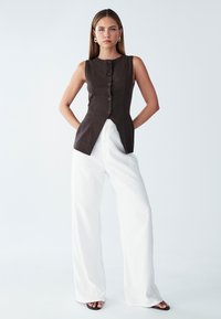 Hnědý bezramínkový top s předními knoflíky, kombinovaný s bílými širokými kalhotami. Hladké textury a přiléhavý střih charakterizují toto oblečení.