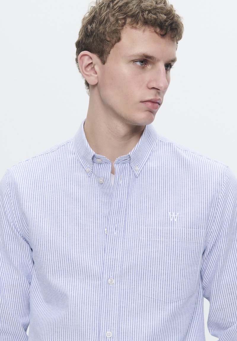 Camisa de botón a rayas azul y blanca con un bolsillo en el pecho, hecha de tela ligera, que presenta un pequeño logo bordado en el bolsillo.