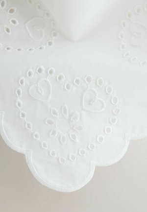 White fabric with scalloped edges featuring embroidered heart and floral patterns in matching white thread.