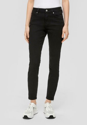 Schwarze Slim-Fit-Jeans aus Denim mit vorderen Taschen, hoher Taille und leicht fransigem Saum an den Knöcheln. Dazu weiße Sneakers.