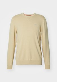 Beige langek mouw crewneck sweater met geribbelde manchetten en zoom, voorzien van een klein logo patch op de linkerborst.