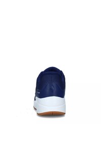 Baskets de sport bleu marine avec une tige en maille texturée, semelle intermédiaire blanche et semelle extérieure en caoutchouc marron. Dispose d'un logo discret près du talon.