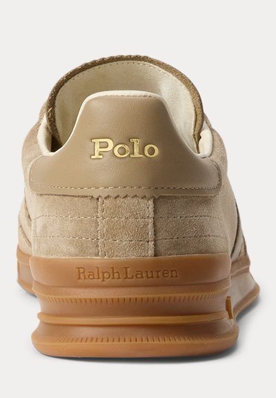 Bėgių batelio kulnas iš smėlio spalvos zomšos, ruda guminė pado dalis, auksinės spalvos užrašas „Polo“ ant odinės kulno viršutinės juostos ir spaustas „Ralph Lauren“ ant pado.