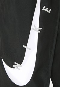 Tela negra con un gran logo de swoosh blanco de Nike, con las letras "N", "I", "K" y "E" en plata, posicionadas verticalmente a lo largo del logo.