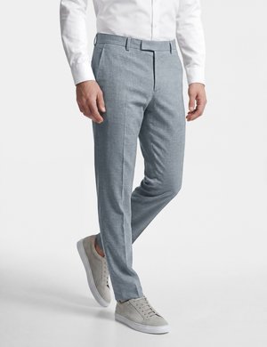 Mann trägt hellgraue, maßgeschneiderte Hose, weißes Hemd und hellgraue Sneaker, steht mit einem leicht angewinkelten Bein.