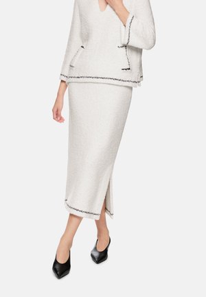 Weißer, strukturierter zweiteiliger Anzug mit einem V-Ausschnitt-Oberteil und einem figurbetonten Rock mit seitlichem Schlitz, verziert mit schwarzem Paspel an den Kanten.