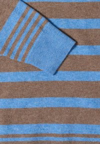 Gros plan d'une manche de pull en maille rayé marron et bleu avec un poignet côtelé et des rayures horizontales assorties sur le corps.