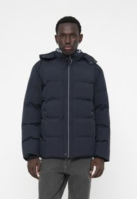 Marineblaue Daunenjacke mit Reißverschluss- und Knopfverschluss, verstellbare Kapuze und schrägen Steppdetails; verfügt über vordere Reißverschluss-Taschen.