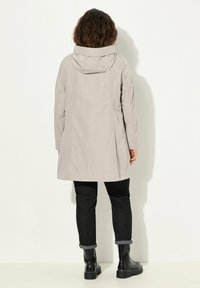 Jasnoszary wodoodporny płaszcz z kapturem, długim rękawem i długości do kolan. Noszony na czarne spodnie i botki za kostkę. Gładka faktura.